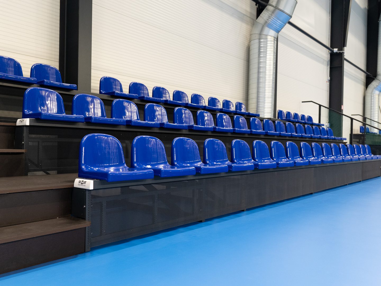 Tribuna s modrými sklopnými sedačkami podél hrací plochy.